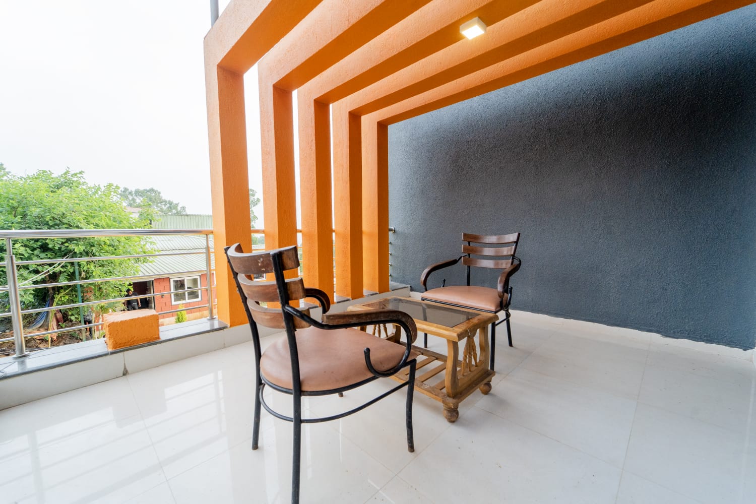 The Tranquil Terrace room balcony with two wooden chairs and a glass-top table against a dark grey wall